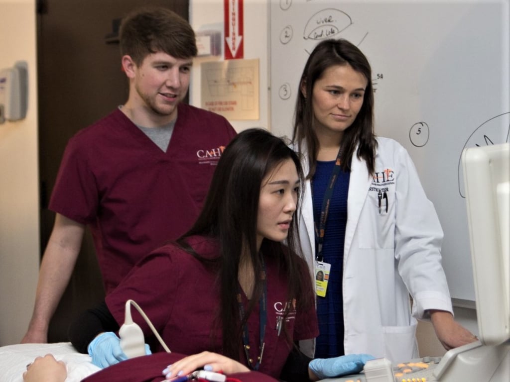 Instructor guiding two sonography students at an ultrasound workstation